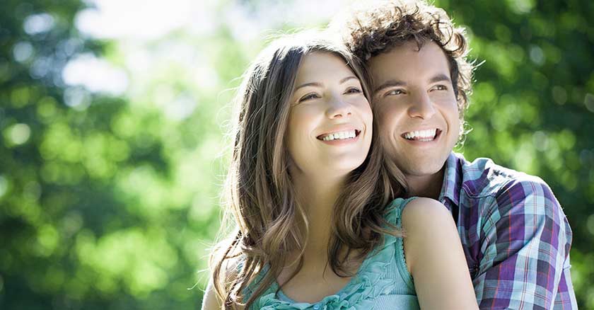 matrimonio pareja de esposos abrazados felices sonriendo mirando fondo arboles